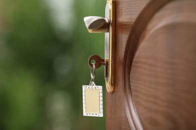 Open door with key on blurred green background, closeup. Space for text