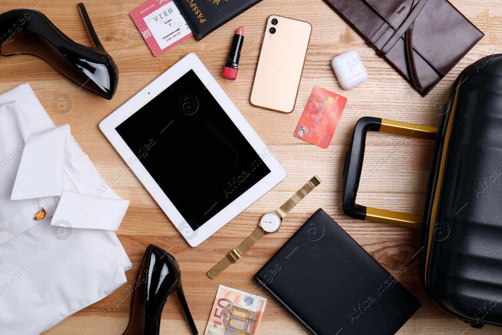 Photo of Business trip stuff and suitcase on wooden surface, flat lay