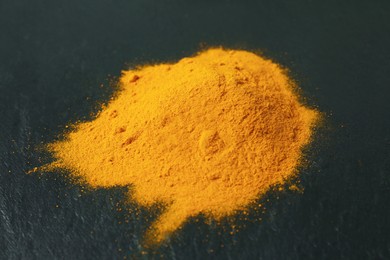 Photo of Turmeric powder on black textured table, closeup