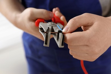 Photo of Professional electrician in uniform stripping wiring, closeup view