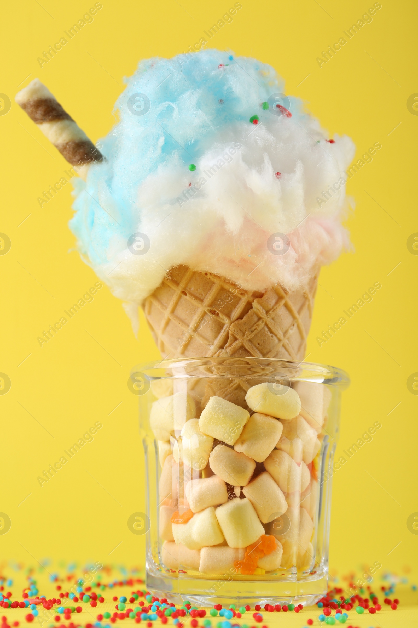 Photo of Sweet cotton candy in waffle cone on yellow background, closeup