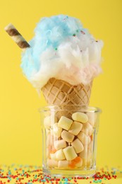 Sweet cotton candy in waffle cone on yellow background, closeup