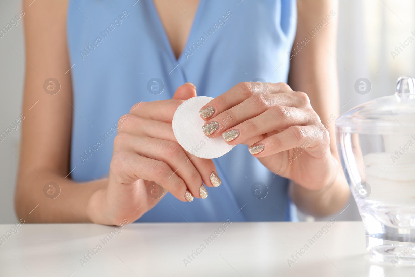 Photo of Woman removing polish from nails with cotton pad at table, closeup