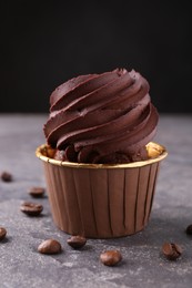 Delicious chocolate cupcake and coffee beans on grey textured table, closeup