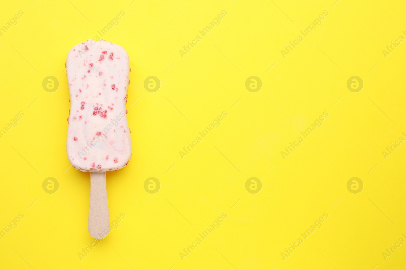 Photo of Delicious glazed ice cream bar on yellow background, top view. Space for text