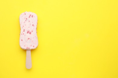 Photo of Delicious glazed ice cream bar on yellow background, top view. Space for text
