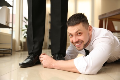 Photo of Man tying shoe laces of his colleague together in office, closeup. Funny joke
