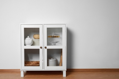 Wooden cabinet with kitchenware near white wall, space for text