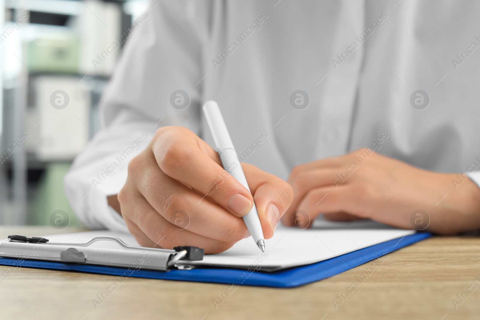 Photo of Woman writing in clipboard with pen at wooden table indoors, closeup