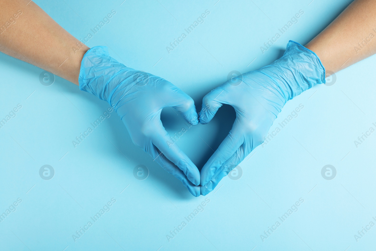 Photo of Doctor wearing medical gloves making heart gesture on light blue background, top view