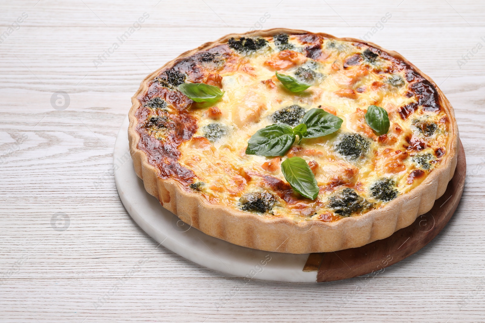 Photo of Delicious homemade quiche with salmon, broccoli and basil leaves on wooden table
