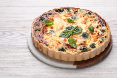 Delicious homemade quiche with salmon, broccoli and basil leaves on wooden table