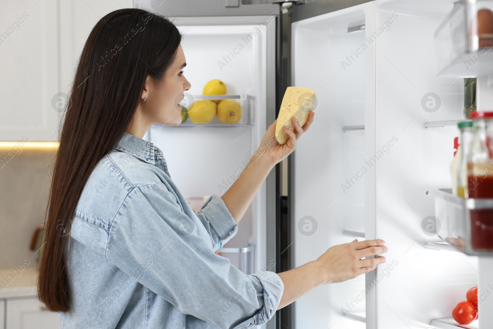 Photo of Young woman taking cheese out of refrigerator in kitchen