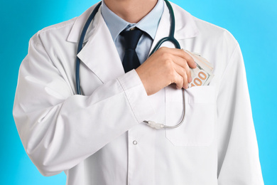 Doctor putting bribe into pocket on light blue background, closeup. Corruption in medicine