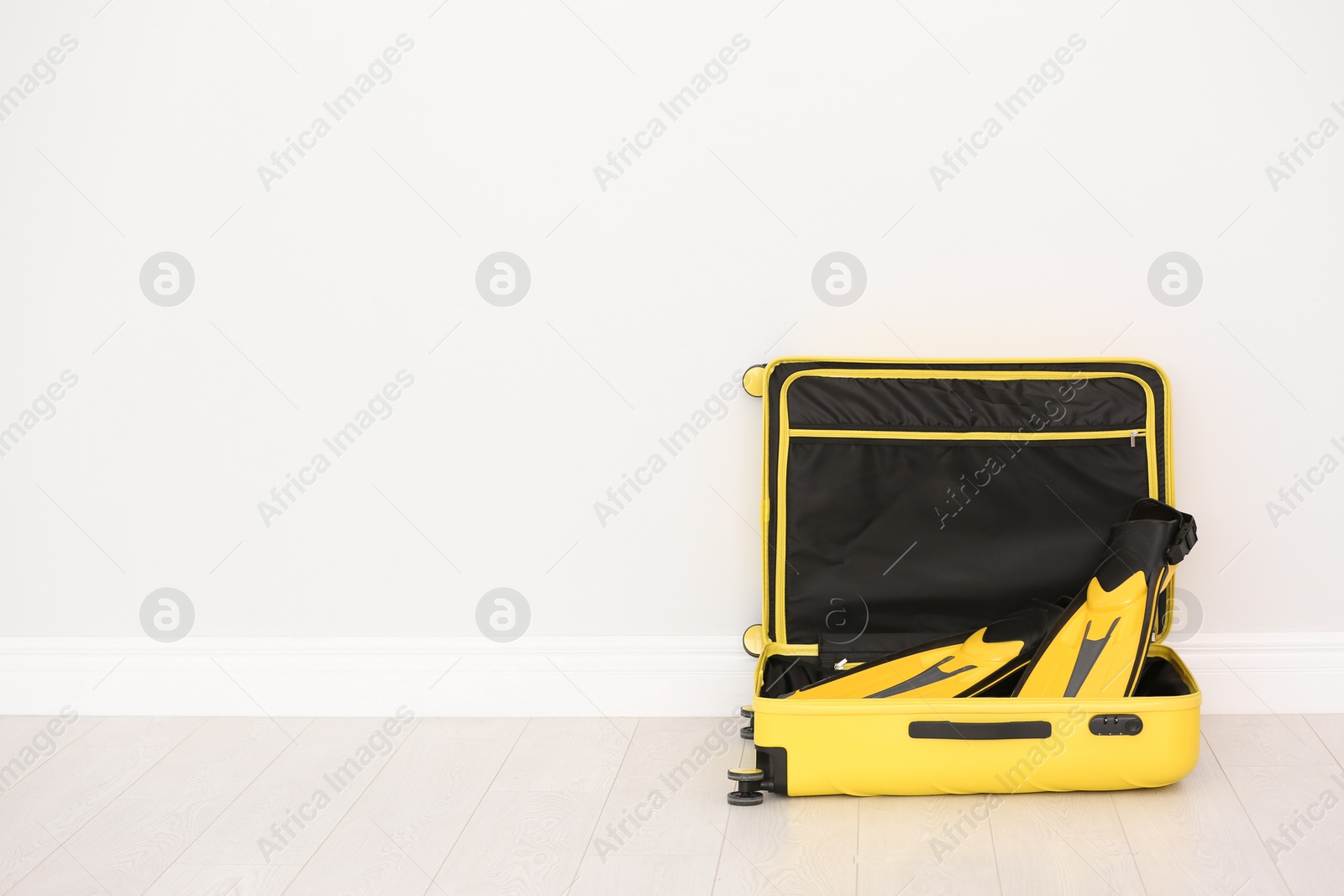 Photo of Modern suitcase with flippers on floor near light wall. Space for text