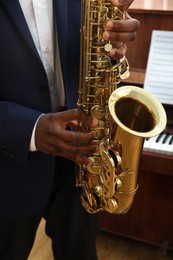 Photo of African-American man playing saxophone indoors, closeup. Talented musician