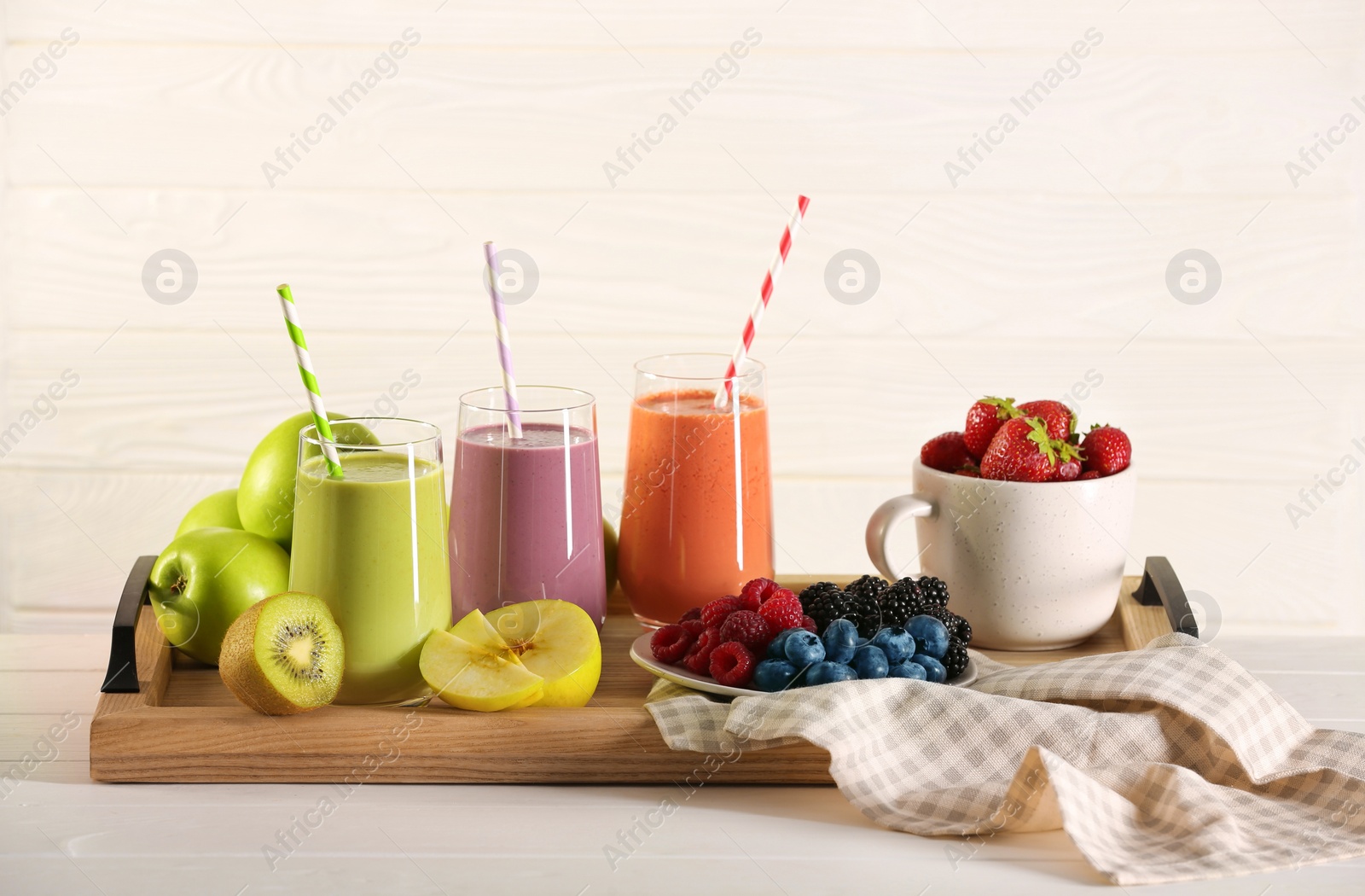 Photo of Glasses of different tasty smoothies and fresh ingredients on white wooden table