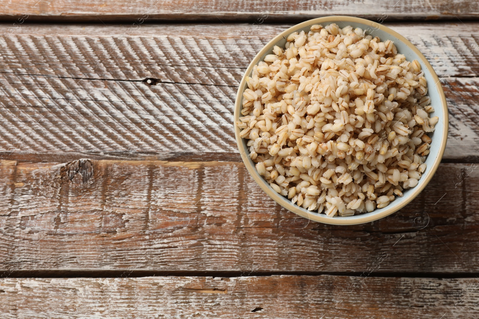 Photo of Delicious pearl barley in bowl on wooden table, top view. Space for text