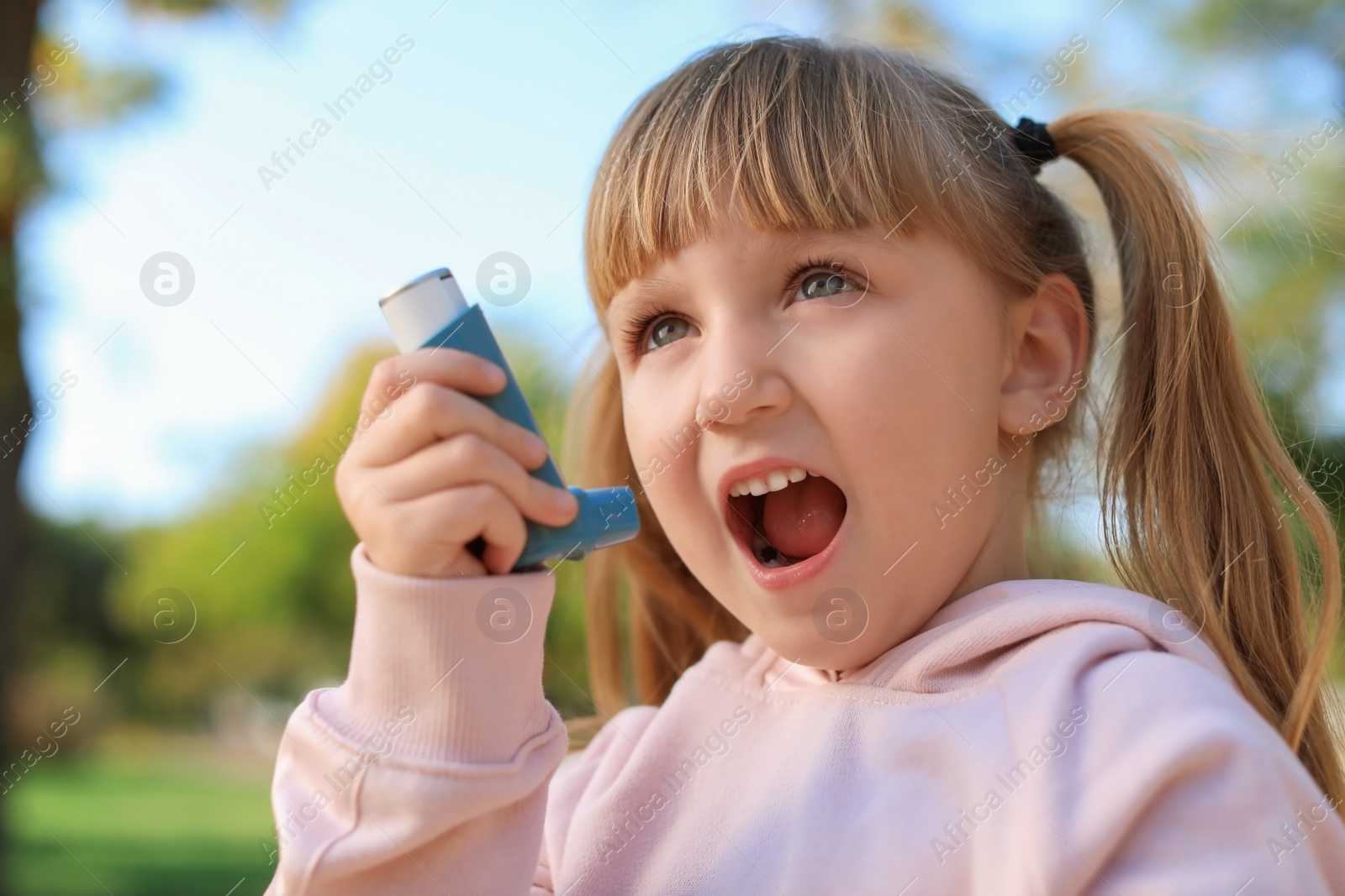 Photo of Little girl using asthma inhaler outdoors. Health care