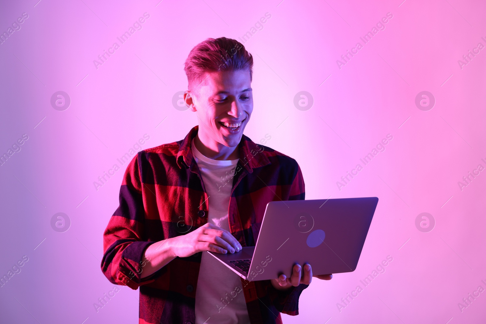 Photo of Young man with laptop talking via video chat on pink background in neon lights