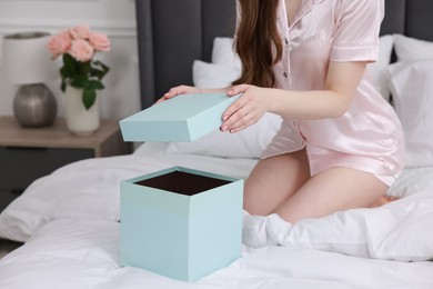 Woman opening gift box on bed in room, closeup. Happy Birthday