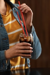 Photo of Woman holding glass of cola with ice against blurred background, closeup