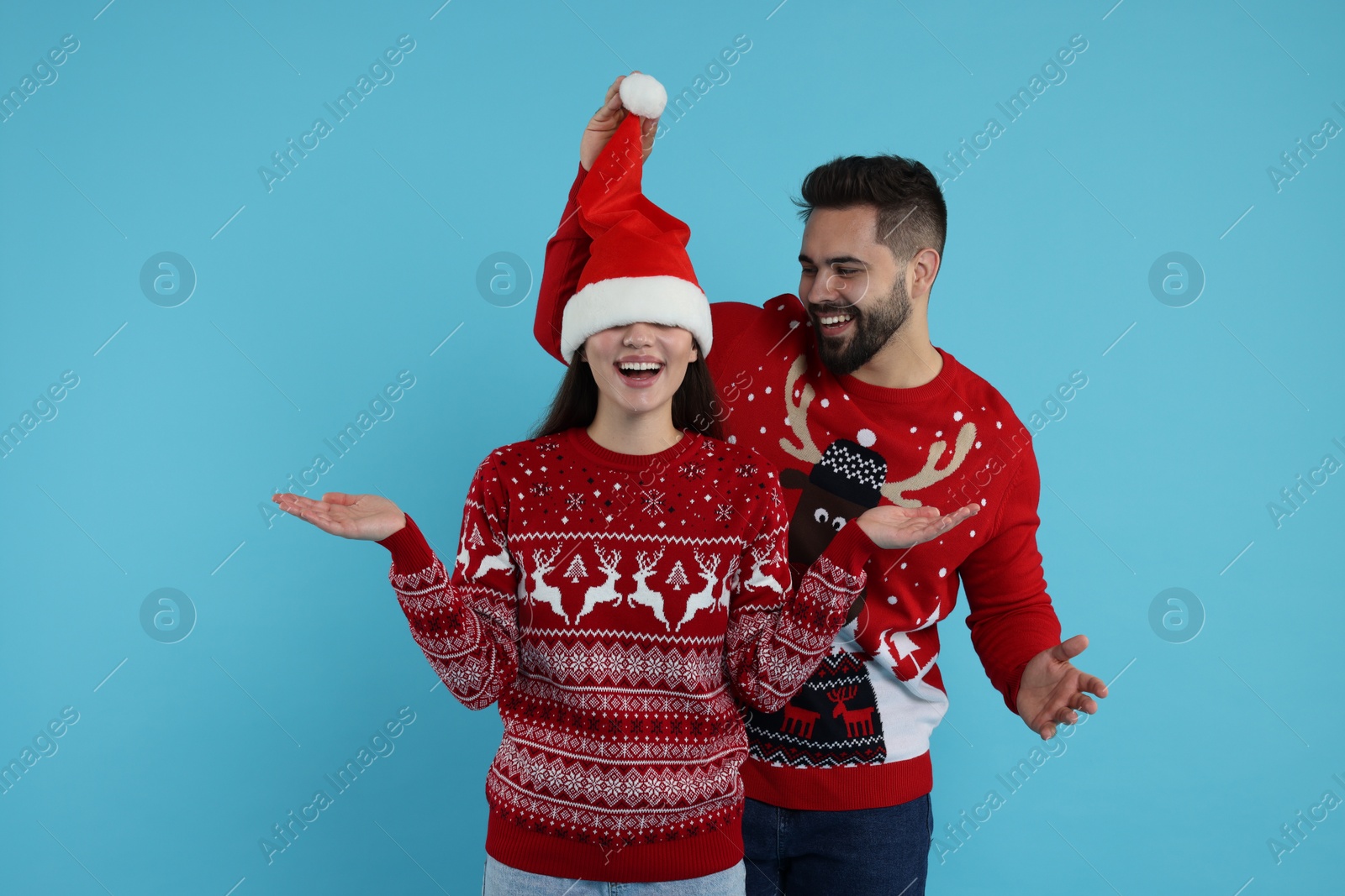 Photo of Happy young couple in Christmas sweaters on light blue background