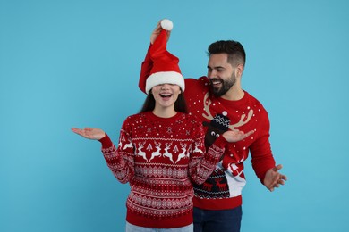 Photo of Happy young couple in Christmas sweaters on light blue background