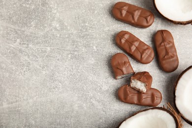 Photo of Delicious milk chocolate candy bars with coconut filling on grey table, flat lay. Space for text