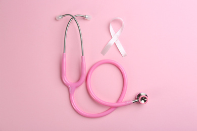 Photo of Pink ribbon as breast cancer awareness symbol and stethoscope on color background, flat lay