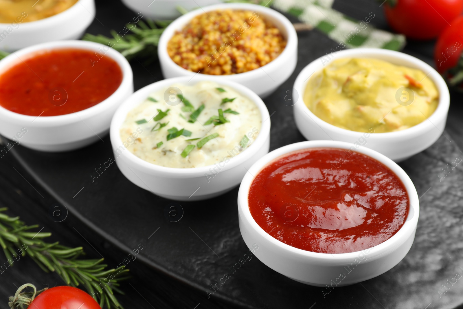 Photo of Different tasty sauces in bowls and rosemary on table, closeup