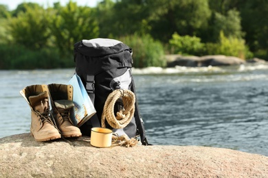 Photo of Backpack and camping equipment on rock near river. Space for text