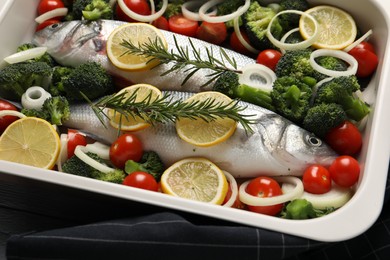 Raw fish with vegetables and lemon in baking dish on table