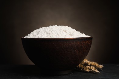 Photo of Wheat flour in bowl and spikes on black table