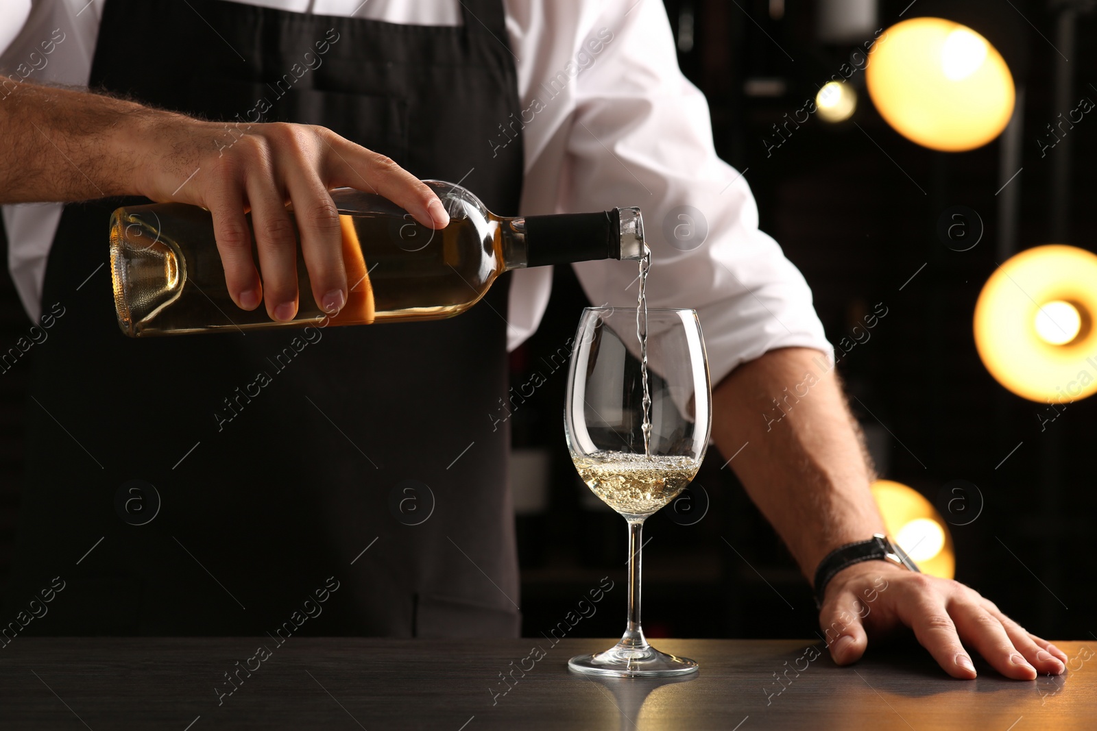 Photo of Bartender pouring white wine into glass at counter indoors, closeup