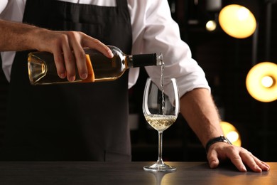 Photo of Bartender pouring white wine into glass at counter indoors, closeup