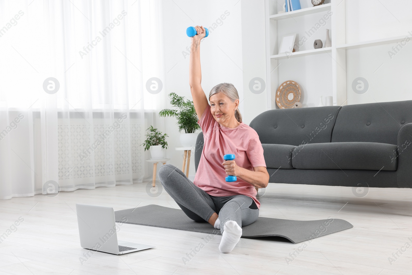 Photo of Senior woman exercising with dumbbells while watching online tutorial at home. Sports equipment