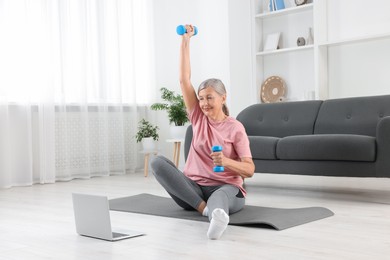 Senior woman exercising with dumbbells while watching online tutorial at home. Sports equipment