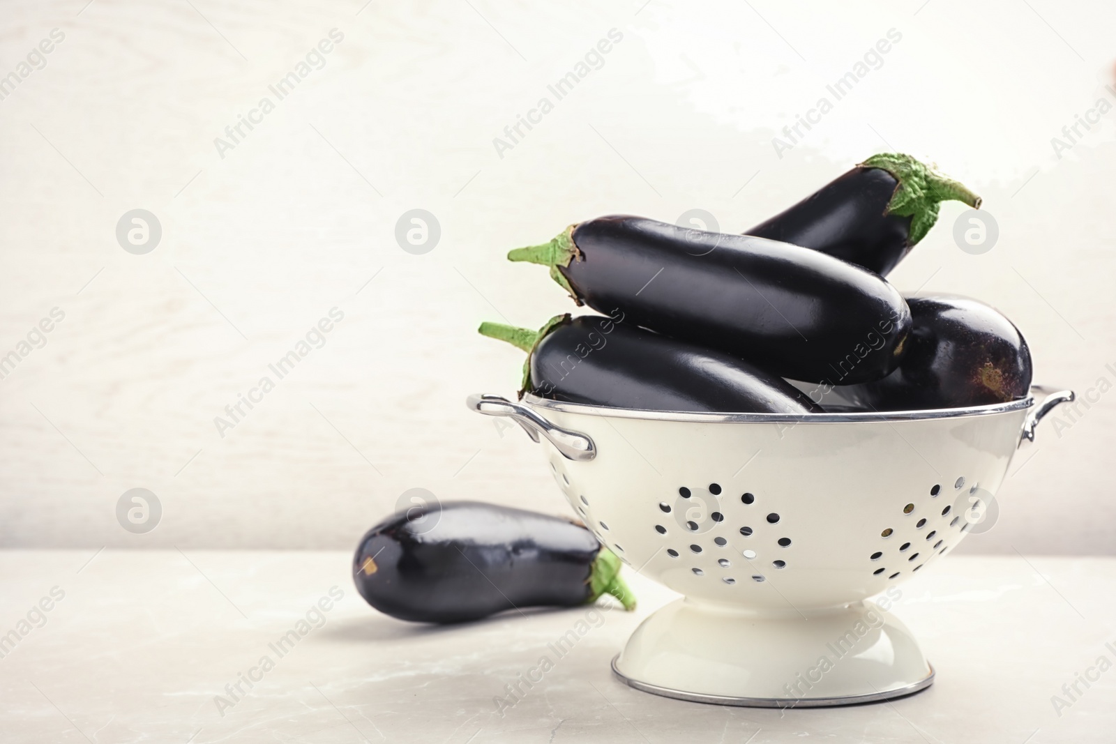 Photo of Colander with eggplants on table against light background