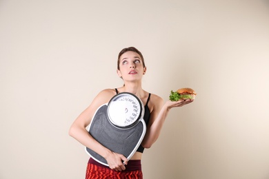 Photo of Young beautiful woman with scales and sandwich on light background. Weight loss motivation