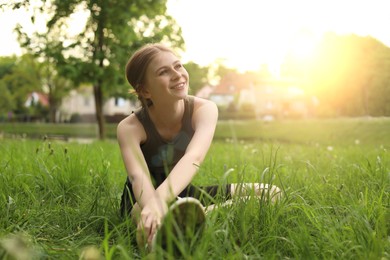 Teenage girl doing morning exercise on green grass in park