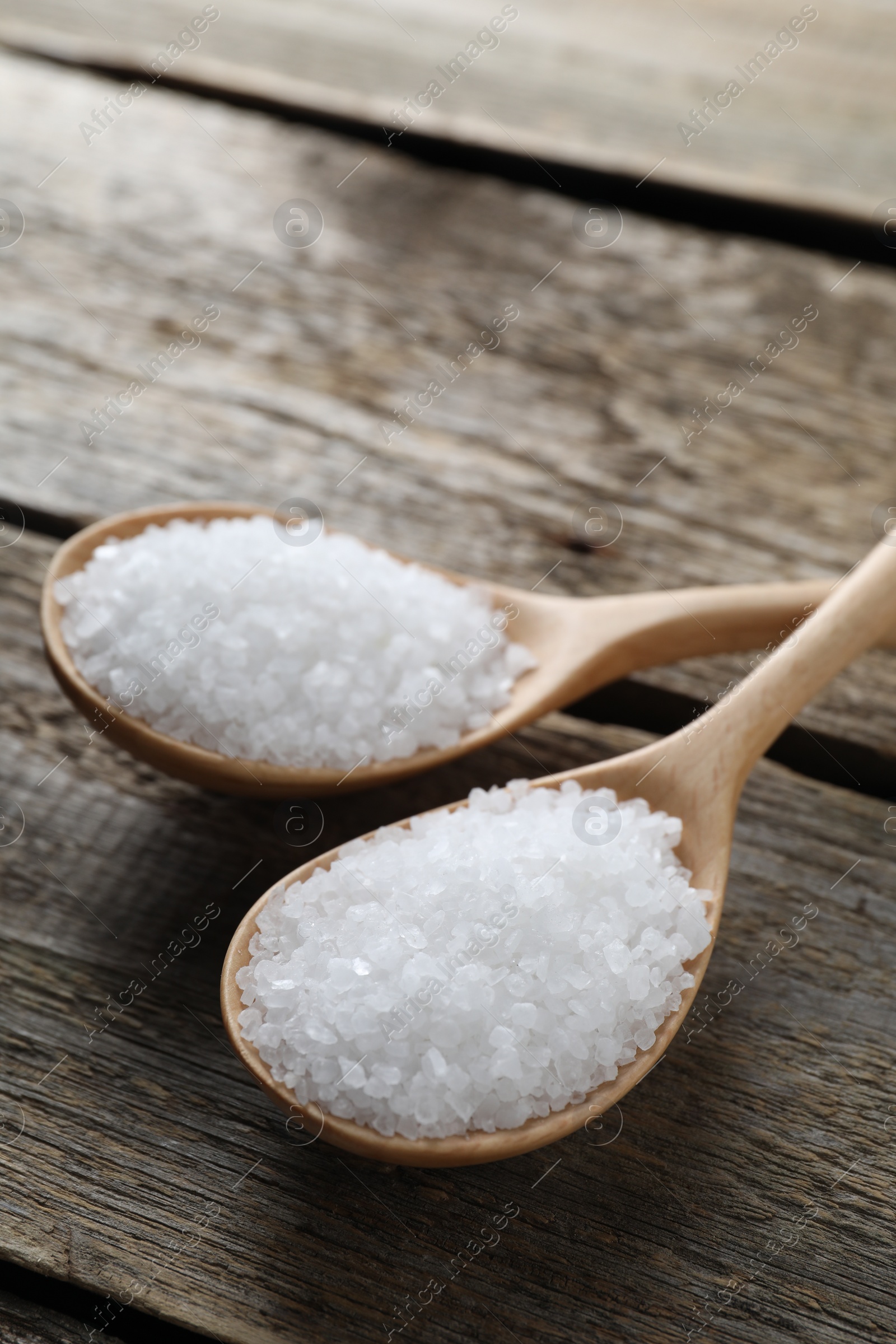 Photo of Organic salt in spoons on wooden table, closeup