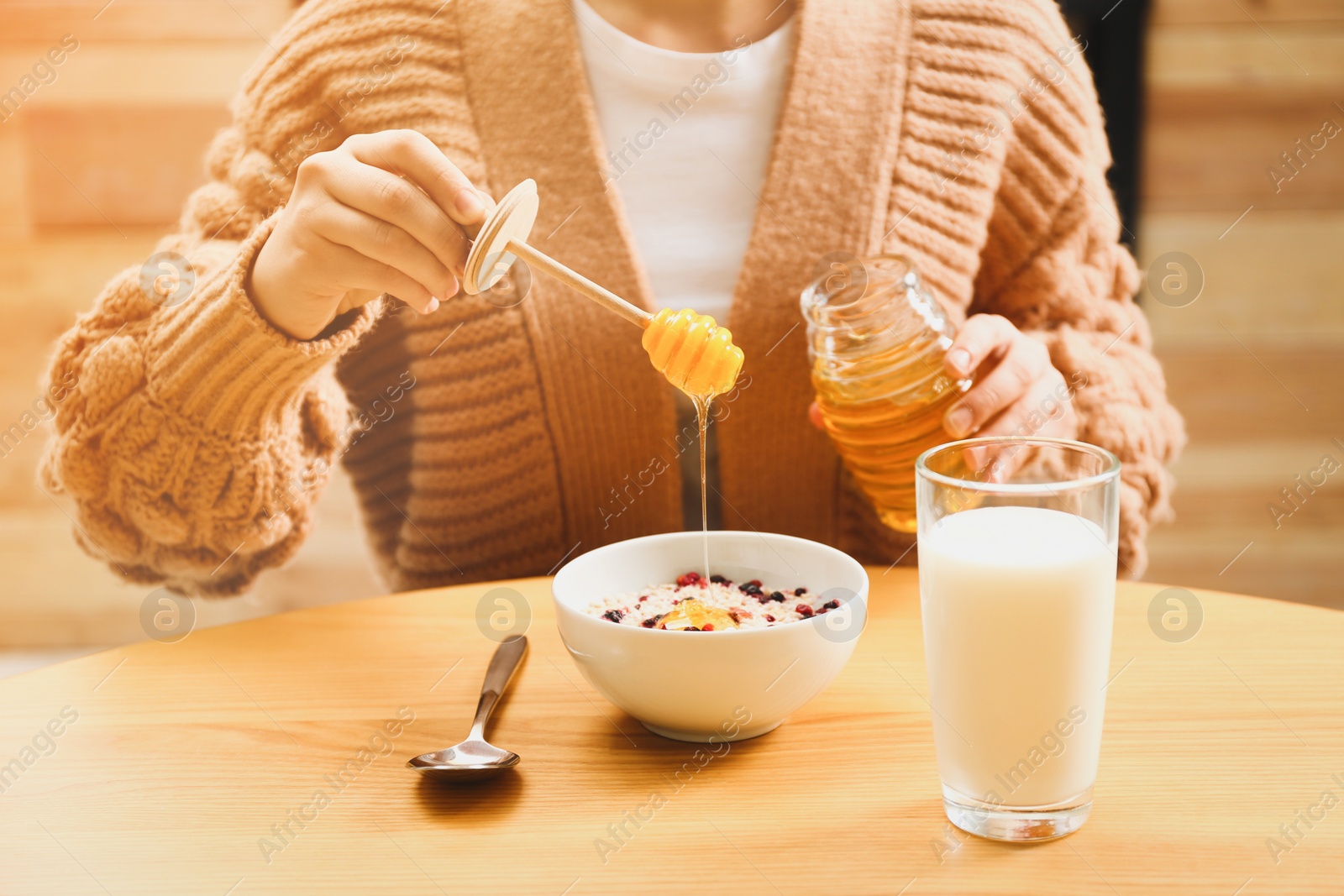 Image of Woman adding honey to oatmeal at wooden table, closeup