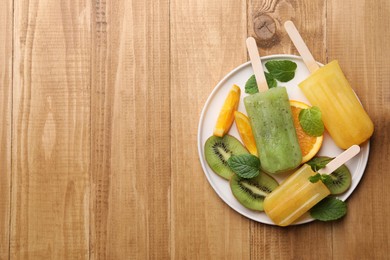 Photo of Plate of tasty orange and kiwi ice pops on wooden table, top view with space for text. Fruit popsicle