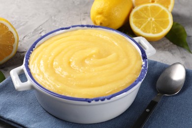 Photo of Delicious lemon curd in bowl, fresh citrus fruits and spoon on grey table, closeup