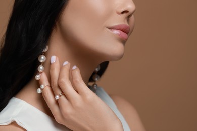 Photo of Young woman wearing elegant pearl jewelry on brown background, closeup