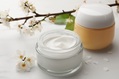 Jars of face cream, leaves, tree branch and flowers on white marble table