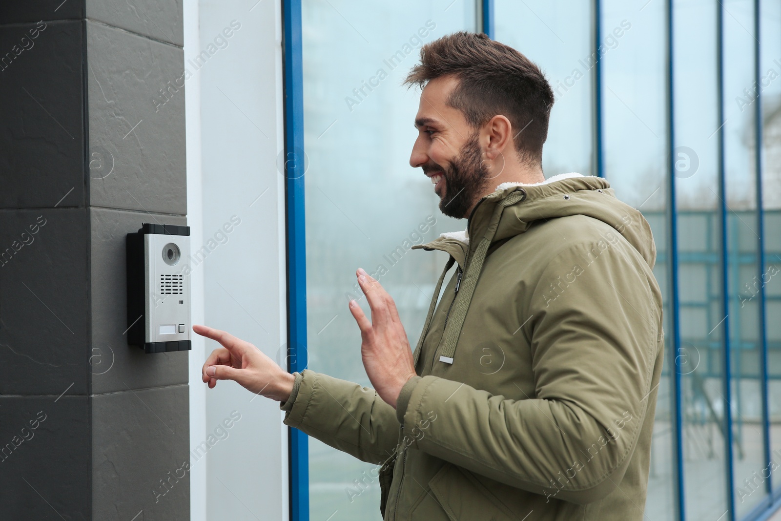 Photo of Happy man ringing intercom while waving to camera near building entrance