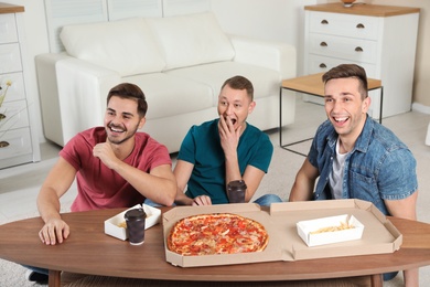 Photo of Group of friends with tasty food laughing while watching TV at home