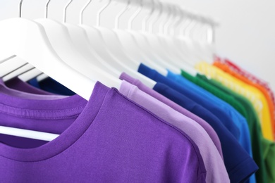 Rack with rainbow clothes on light background